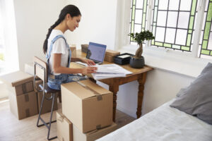 Woman sitting at a desk with moving boxes representing work-from-home moving patterns.