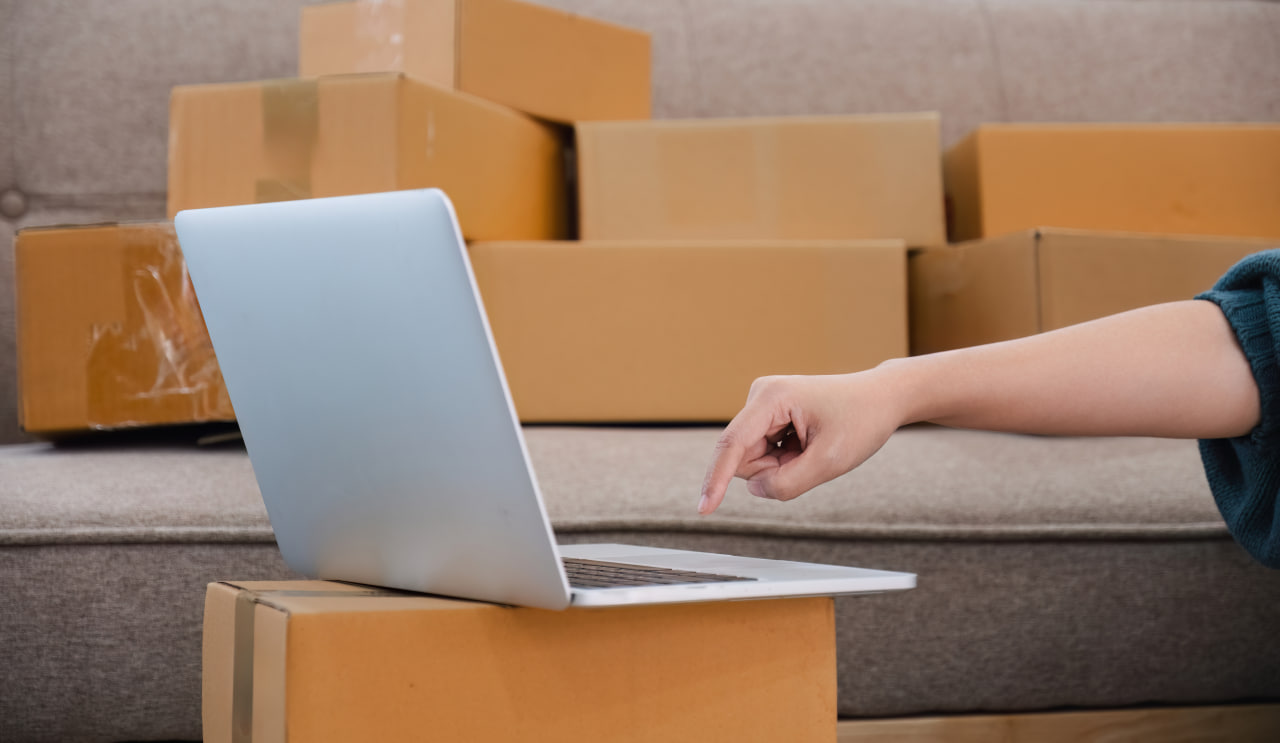 Person with a laptop and boxes ordering moving subscription boxes through a packing supplies subscription.