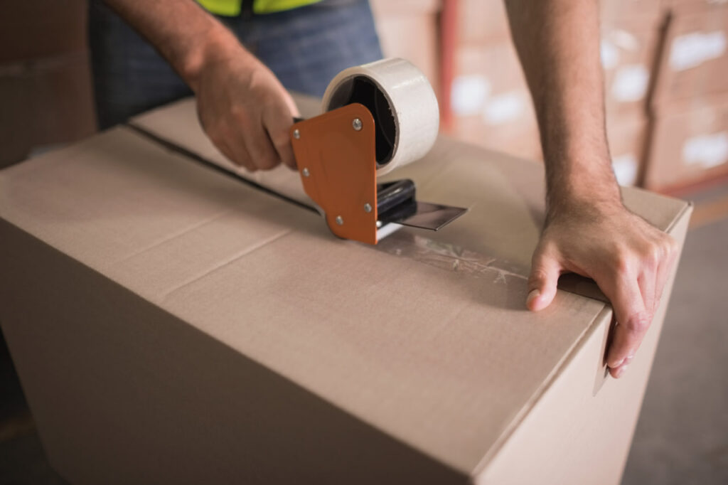 Close up of a person taping a box with items from their packing supplies subscription.