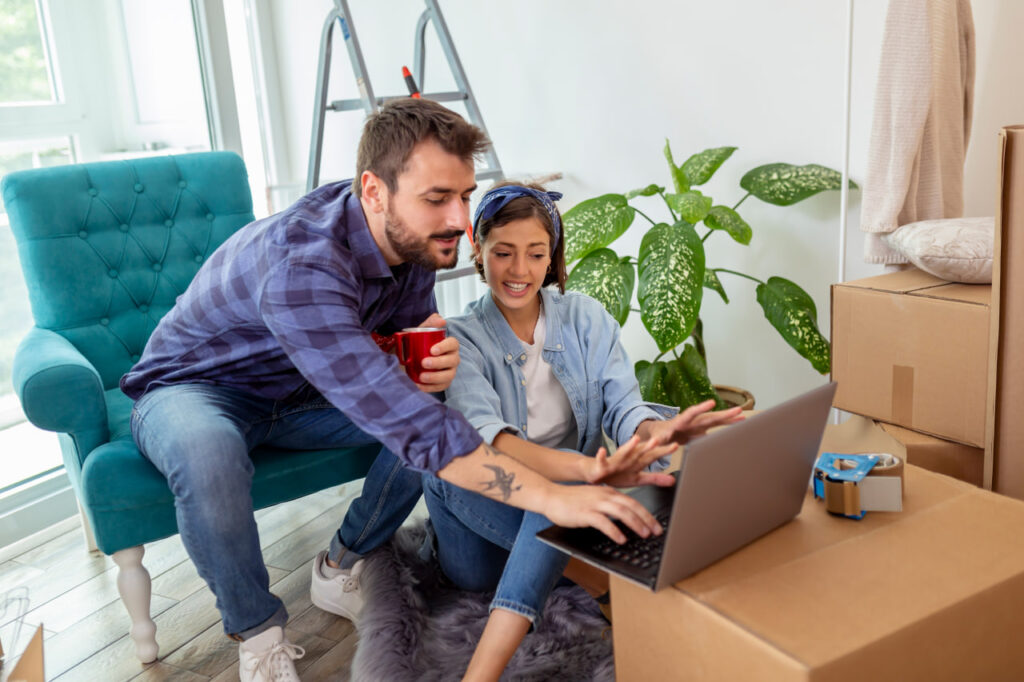 Young couple with a moving box, trying to vet rental home remotely by following online apartment hunting tips.