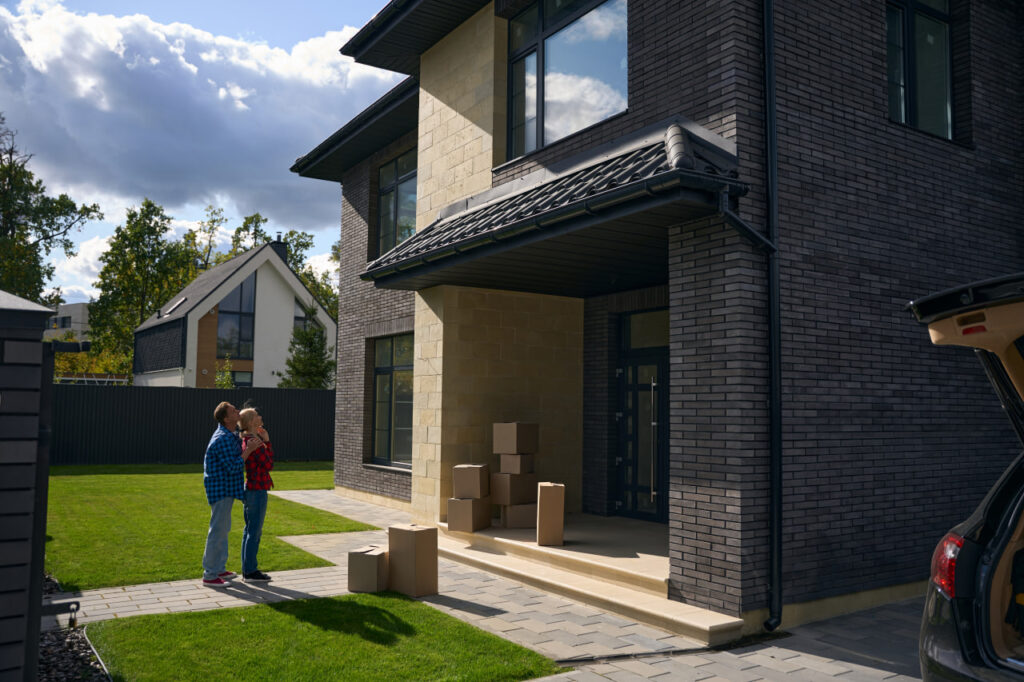 Excited couple standing in front of their new home after completing moving day prep.
