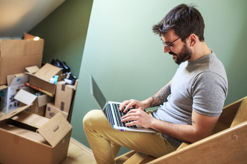 Young man working on his computer surrounded by boxes, considering an instant moving estimate for a moving company quote.