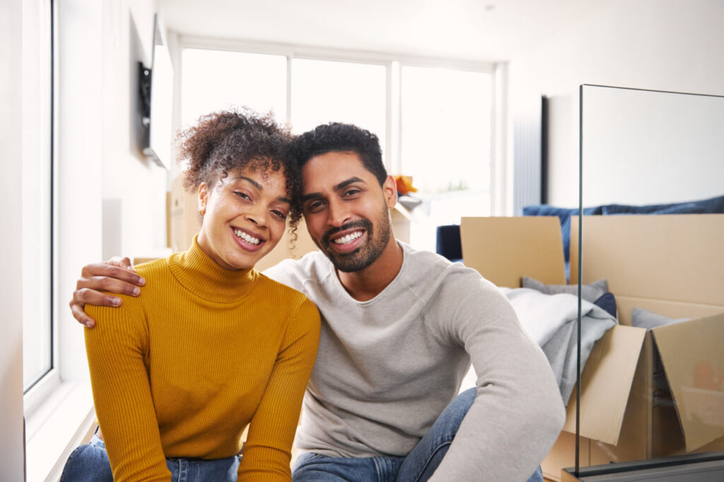 A happy seated couple surrounded by moving boxes know how to save money on a professional move.